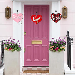 Pink door with decorative hearts and flower pots on a white wall.