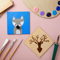 Paintings of a fox and a deer on a pink surface with art supplies.
