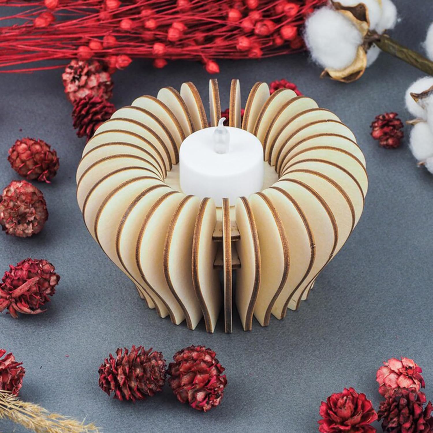 Wooden candle holder with a white candle surrounded by red and white decorative elements on a dark surface.