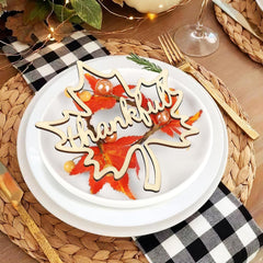 Thankful sign on a white plate with autumn leaves, checkered napkin, and wine glass.