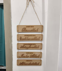 Wooden plaque with engraved phrases on a white wall.