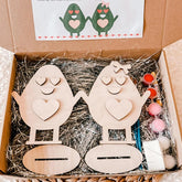 Wooden egg-shaped characters with heart designs in a box with straw padding.