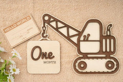 Wooden excavator-shaped milestone with 'One' and 'Monte' text on a beige background.