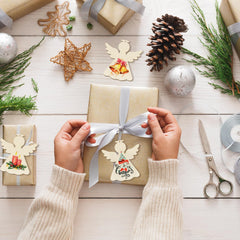 Person wrapping a gift with angel decorations on a wooden surface.