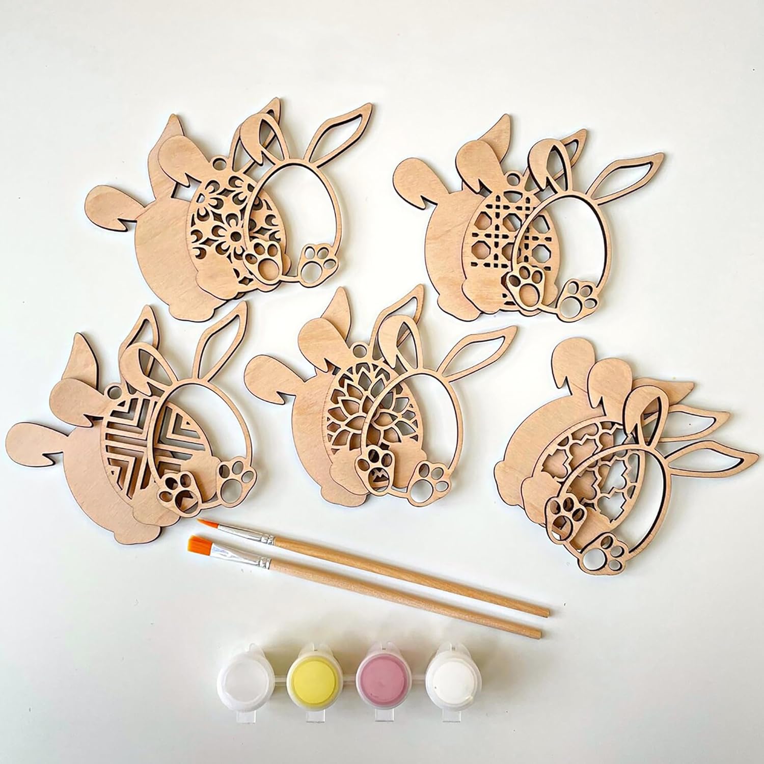 Wooden bunny shapes with paintbrushes and paint on a white background