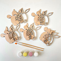 Wooden bunny shapes with paintbrushes and paint on a white background