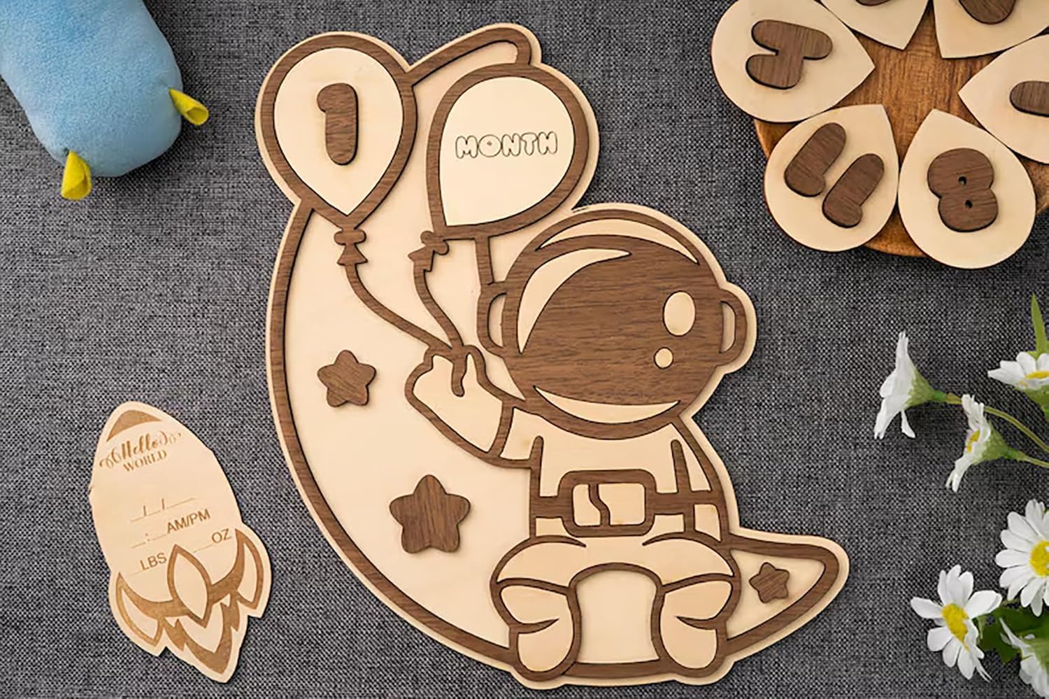 Wooden baby milestone card with space-themed design on a textured surface.