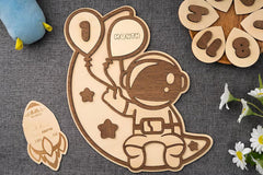 Wooden baby milestone card with space-themed design on a textured surface.