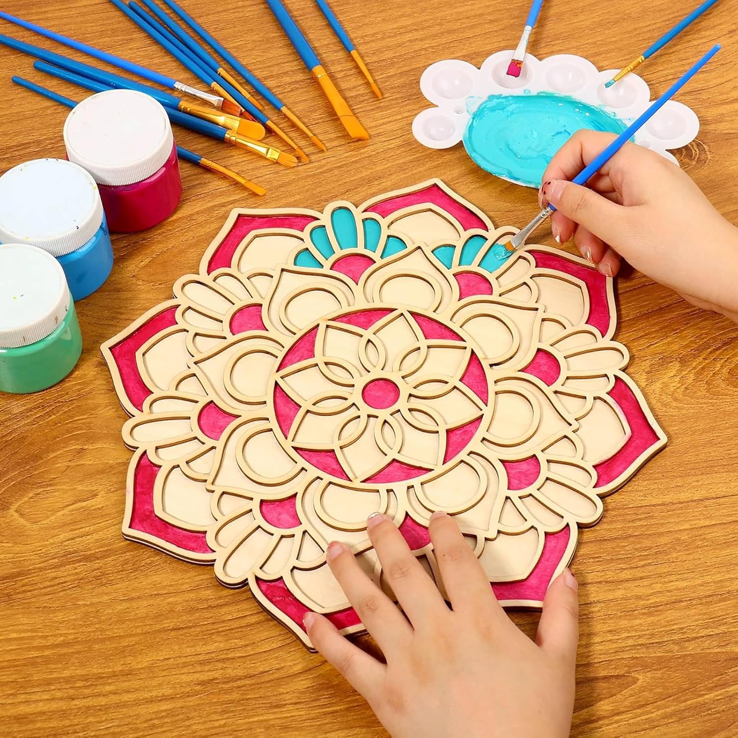 Wooden mandala being painted with colorful paint and brushes on a wooden table.