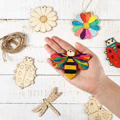 Hand holding a colorful bee ornament with wooden templates on a white wooden surface.