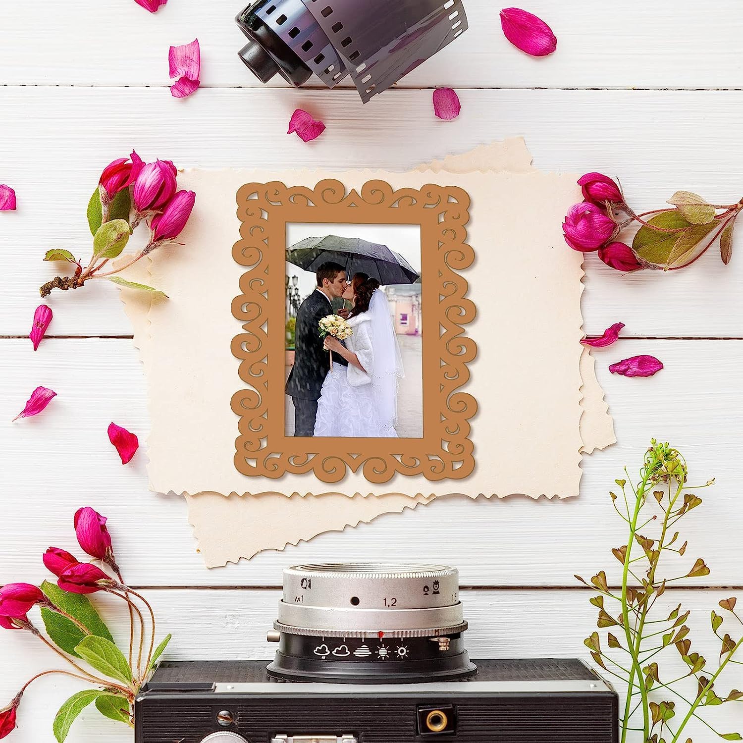 Decorative photo frame with a couple picture, surrounded by flowers and a vintage camera on a wooden surface.