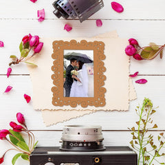Decorative photo frame with a couple picture, surrounded by flowers and a vintage camera on a wooden surface.