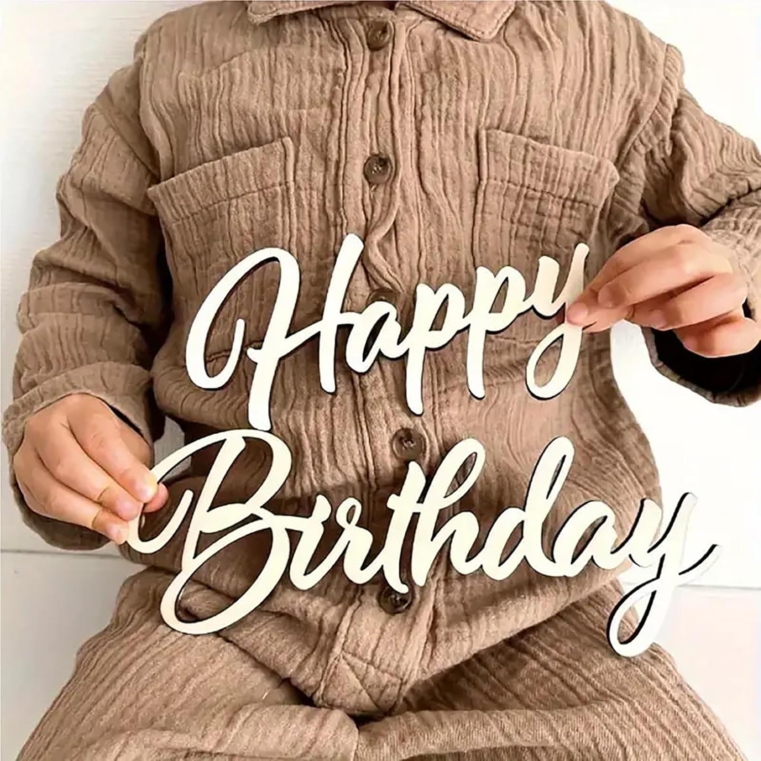 Person wearing a beige corduroy jacket holding a 'Happy Birthday' sign.