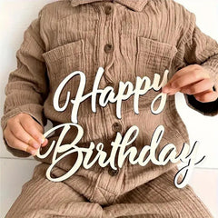 Person wearing a beige corduroy jacket holding a 'Happy Birthday' sign.