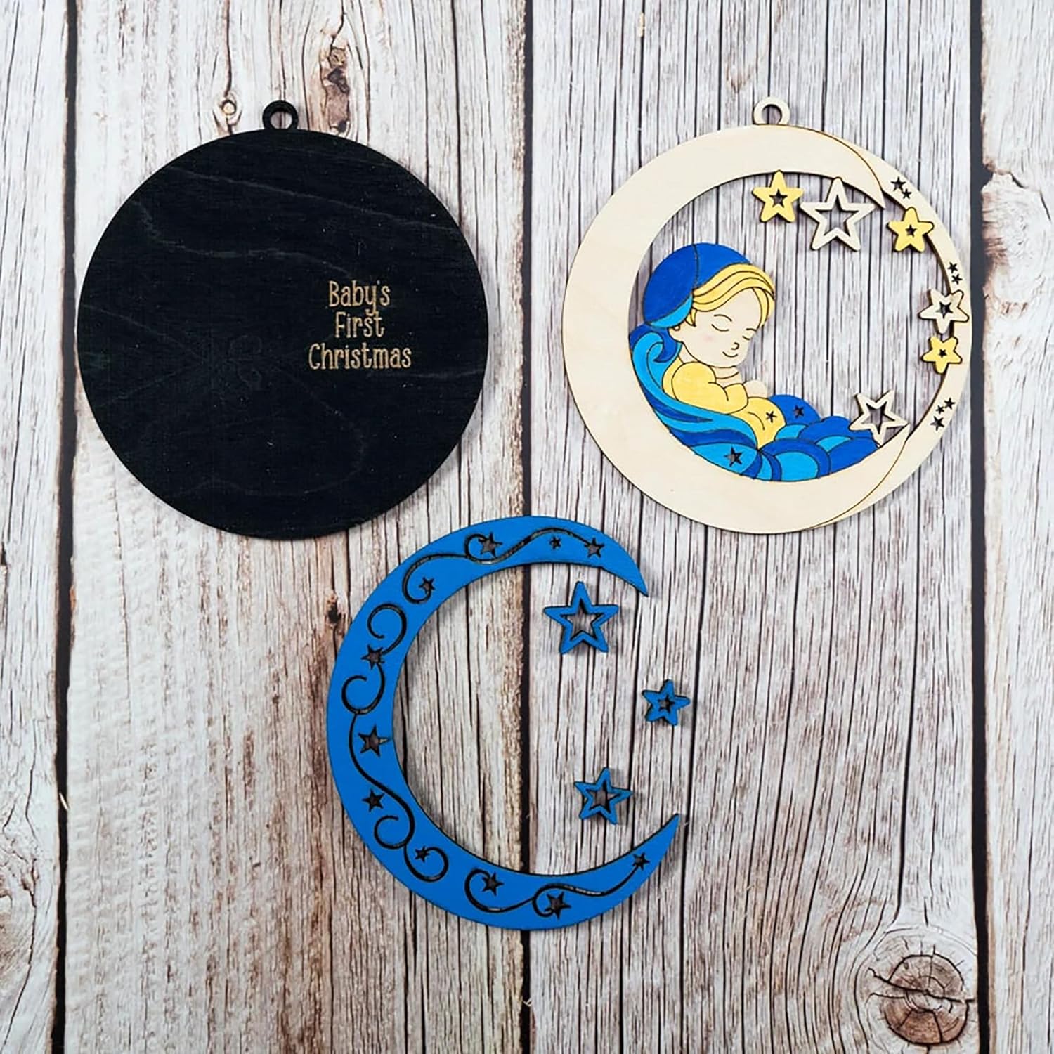 Decorative baby ornaments on a wooden surface, including a black round ornament and two crescent moon designs.