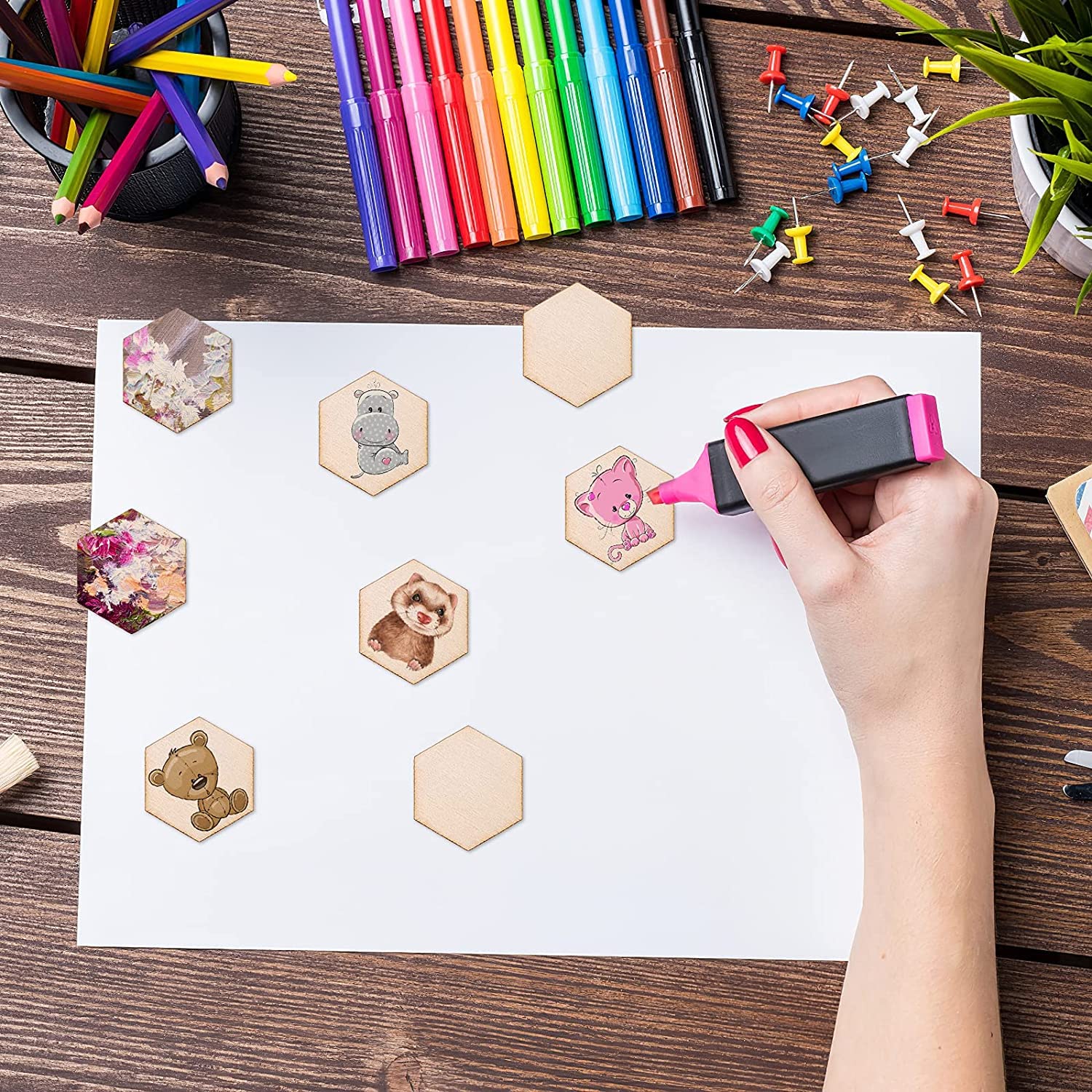 Hand using a stamp on a piece of paper with hexagonal stamps, surrounded by colorful markers and pins on a wooden surface.