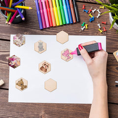 Hand using a stamp on a piece of paper with hexagonal stamps, surrounded by colorful markers and pins on a wooden surface.