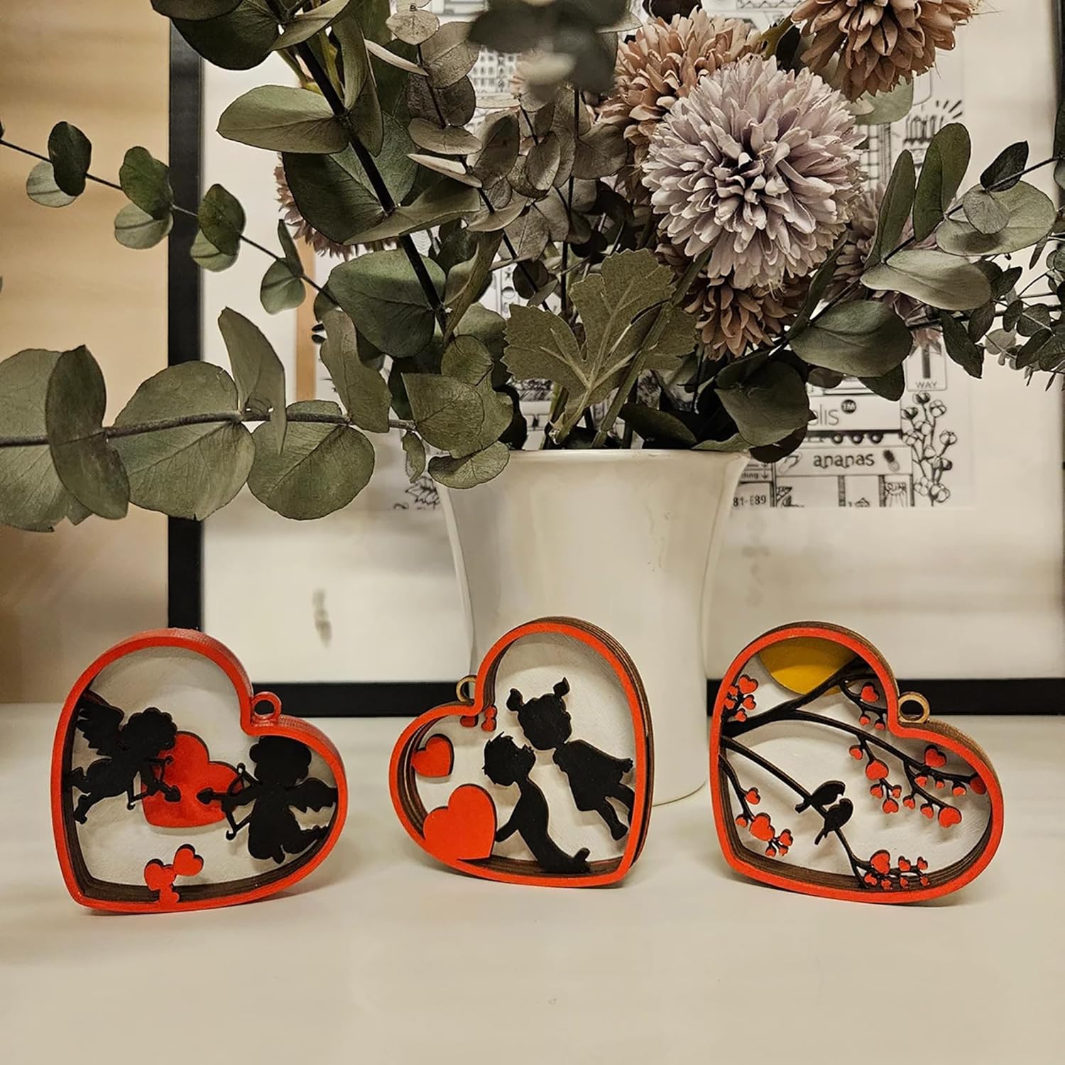 Heart-shaped decorative items with silhouettes of a couple and a heart, placed in front of a vase with flowers.