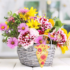Bouquet of colorful flowers in a woven basket with an Easter tag on a light background