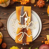 Thanksgiving table setting with 'thankful' sign, knife, fork, and yellow napkin on a wooden background.