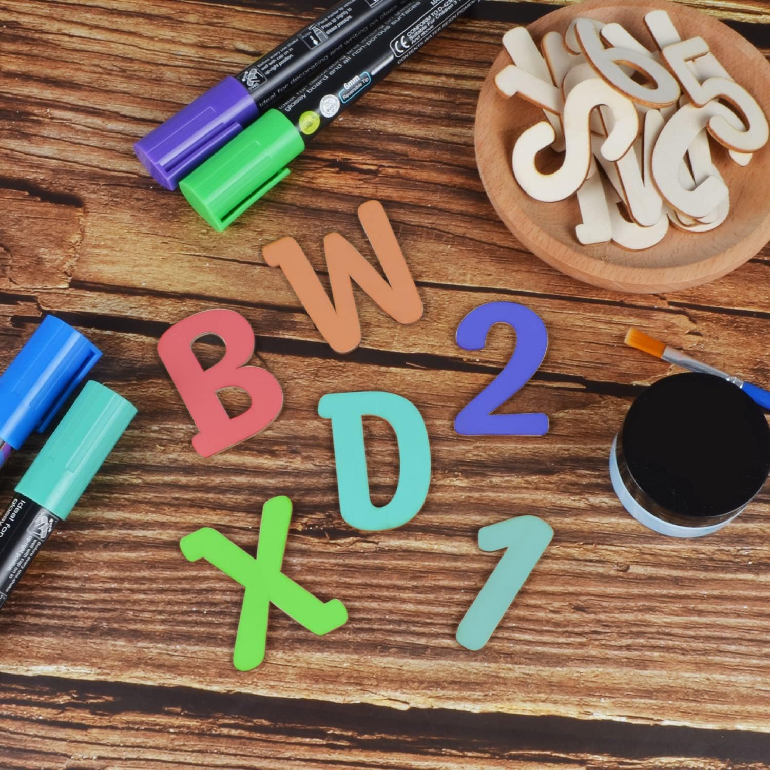 Colorful magnetic letters and numbers on a wooden surface with markers and a bowl of additional letters.