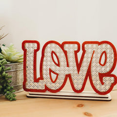 Decorative sign with 'LOVE' on a wooden surface with plants in the background