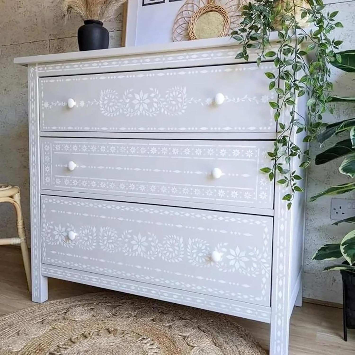 White dresser with decorative patterns in a room with plants and a rug.