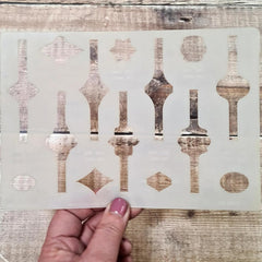 Decorative stencil with geometric patterns held by a hand on a wooden surface