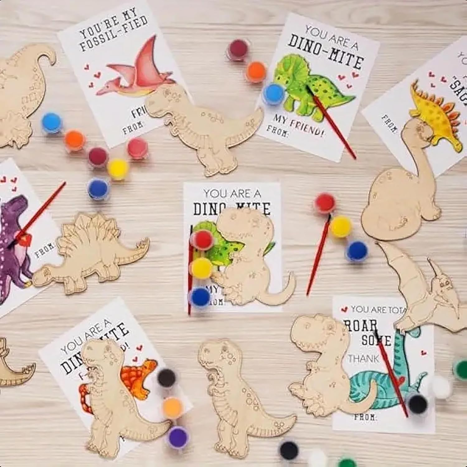 Wooden dinosaur shapes with cards and paint supplies on a wooden surface