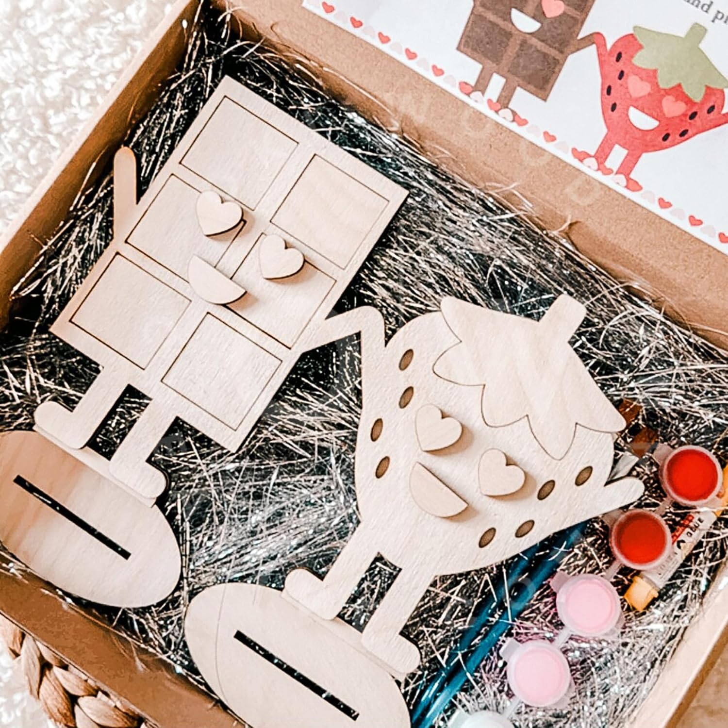 Wooden craft items and paint cans in a box with straw bedding