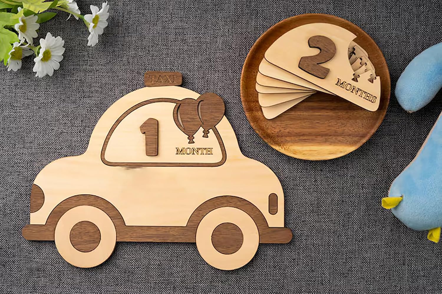 Wooden baby milestone cards with car and flower decorations on a textured surface