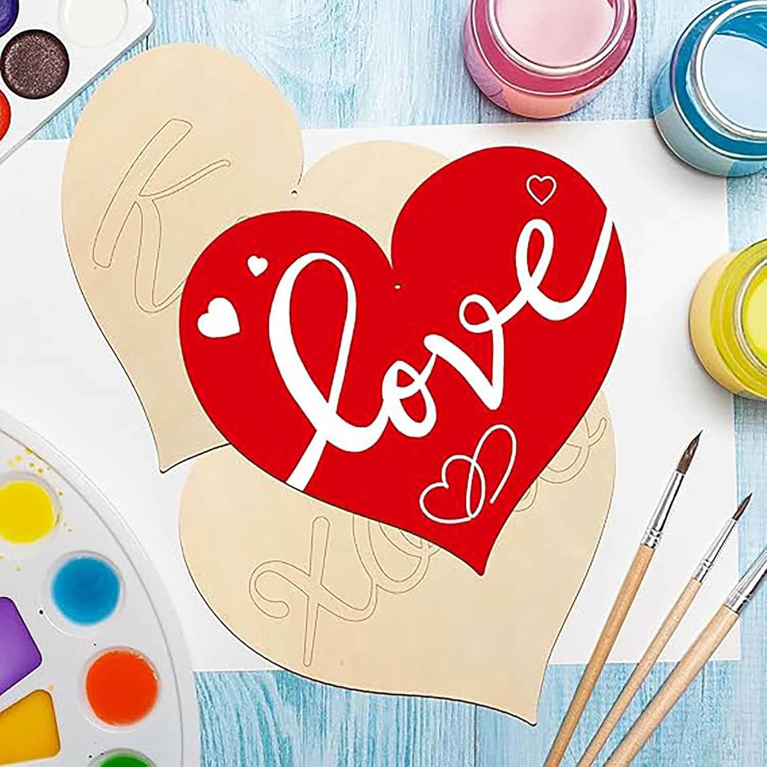 Heart-shaped wooden cutout with 'love' text on a blue surface with paint supplies.