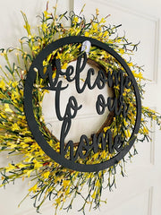 Decorative wreath with yellow flowers and 'Welcome to our home' text on a white door.
