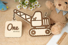 Wooden construction vehicle milestone with 'One Month' tag, teddy bear, and flowers on a textured surface.