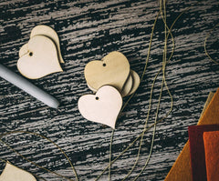 Heart-shaped wooden earrings on a textured surface with a pen and book in the background.