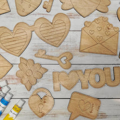 Wooden heart-shaped and letter cutouts on a wooden surface with paint tubes.