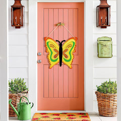 Pink door with a colorful butterfly decoration, green watering can, and planters on a white wall.