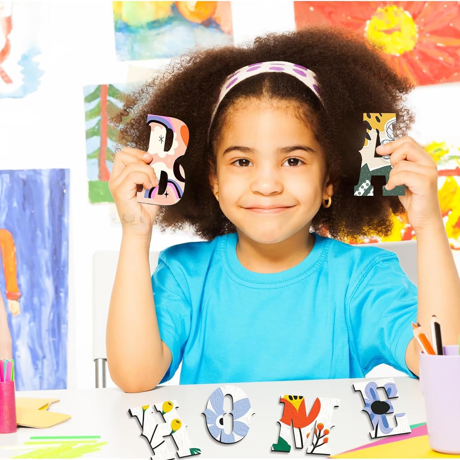Child holding up colorful letters in front of a wall with art projects