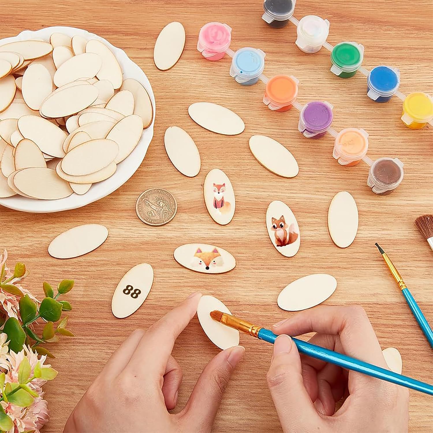 Crafting activity with wooden shapes, paint containers, and a hand painting a small object on a wooden table.