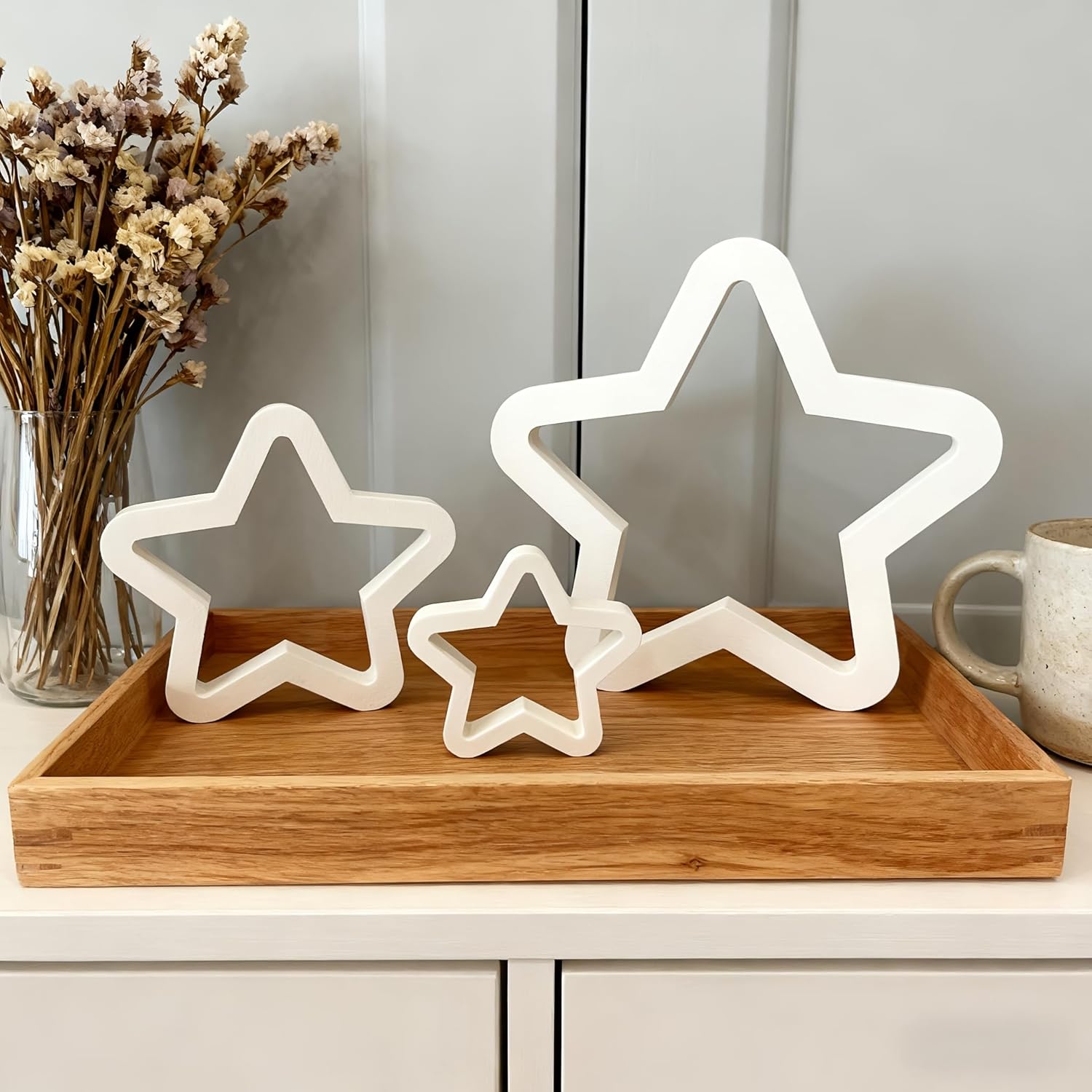 White star-shaped lights on a wooden tray with a vase of dried flowers and a mug in the background.