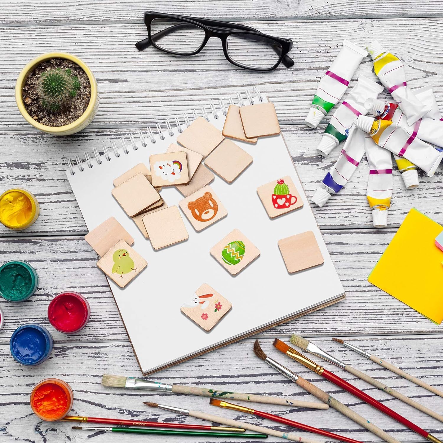 Artistic setup with wooden stamps, paint containers, brushes, and a notebook on a wooden surface.