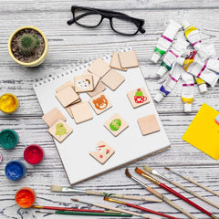 Artistic setup with wooden stamps, paint containers, brushes, and a notebook on a wooden surface.