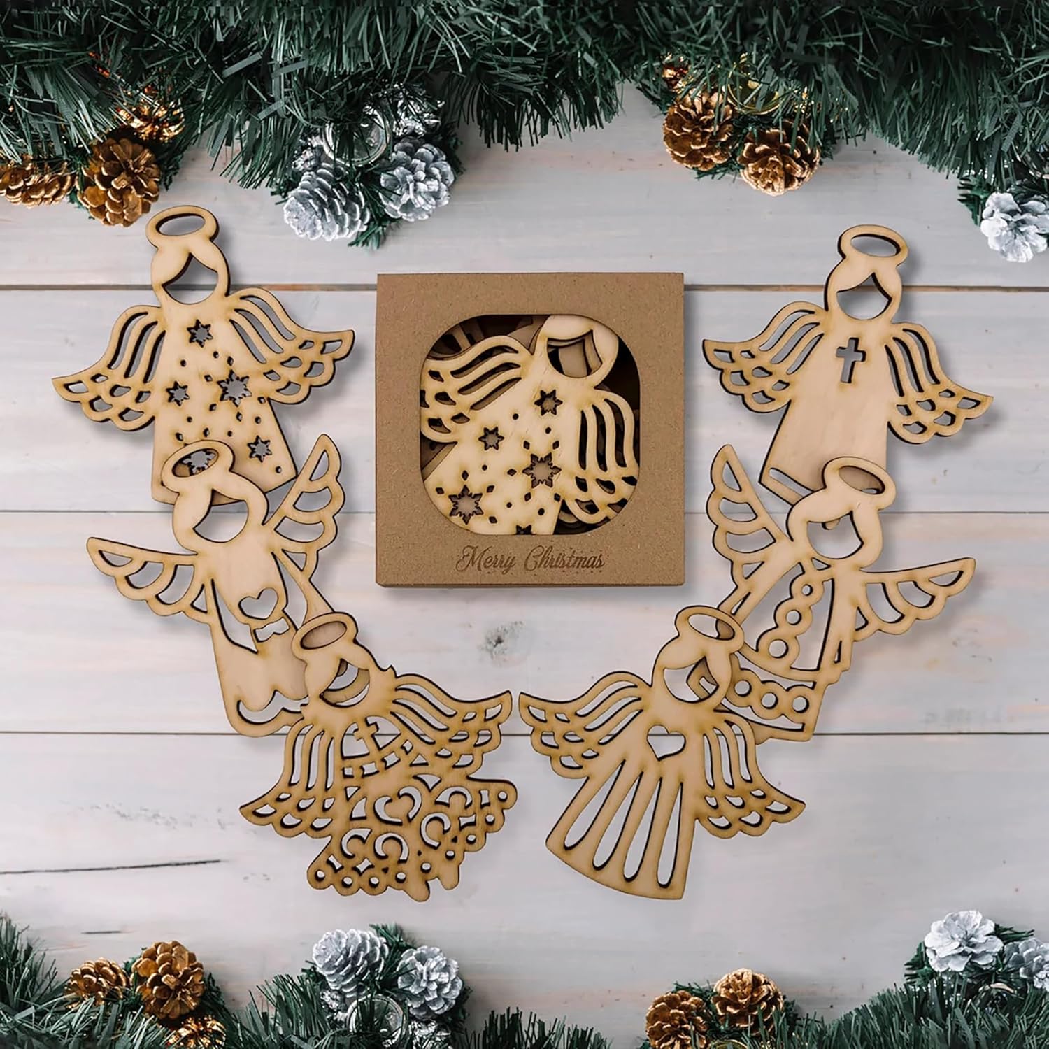 Wooden angel decorations with a 'Merry Christmas' box on a wooden surface with Christmas tree branches.