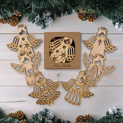 Wooden angel decorations with a 'Merry Christmas' box on a wooden surface with Christmas tree branches.
