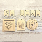 Wooden decorations with 'BE MINE' banner, heart design, 'LOVE' tag, and 'XO' emblem on a wooden surface.
