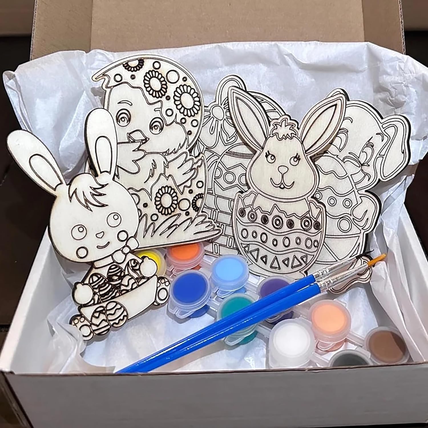 Box with wooden cutouts of rabbits and chicks, paint bottles, and brushes for painting.