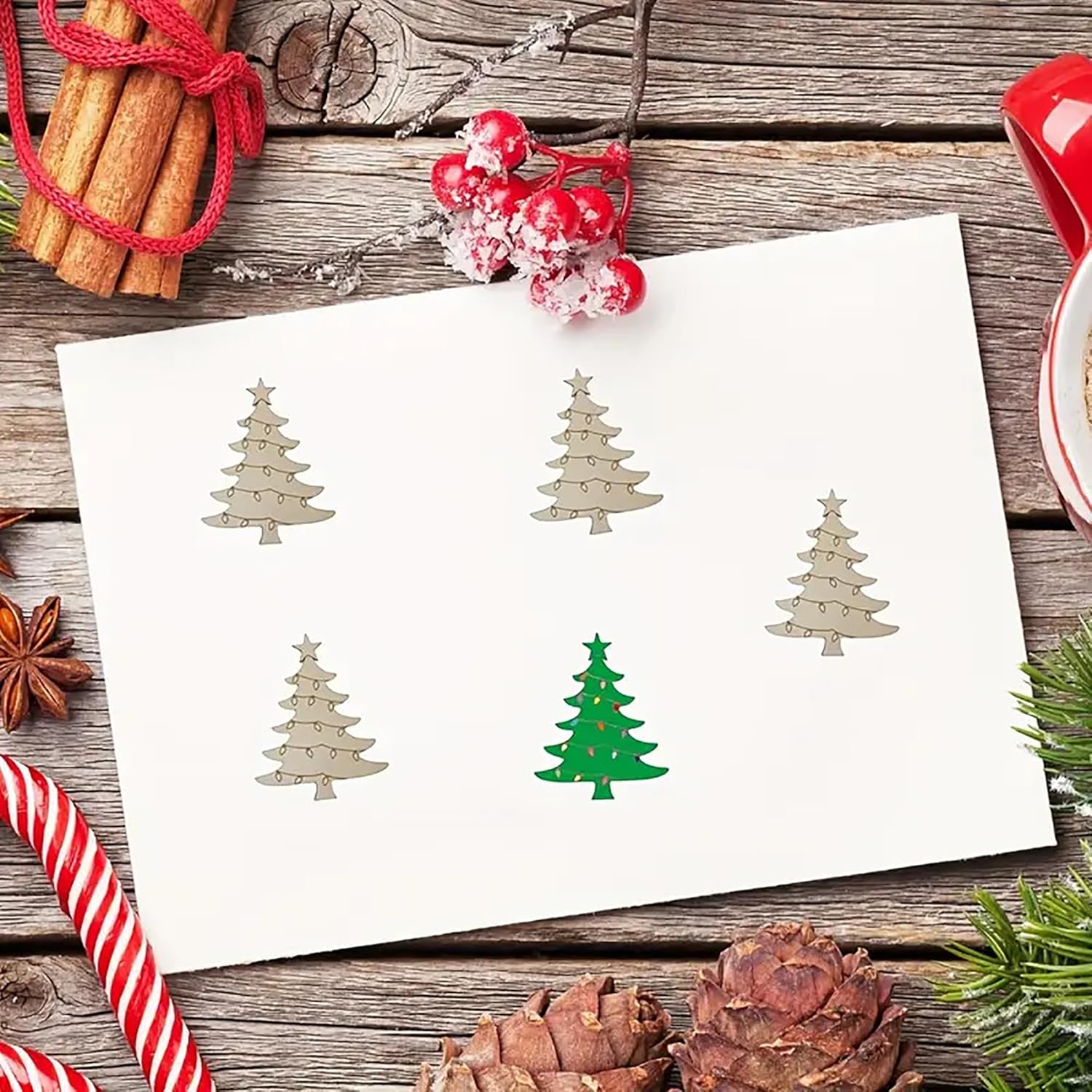 Sheet of paper with Christmas tree cutouts on a wooden surface with holiday decorations.