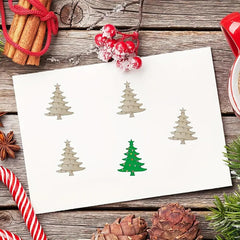 Sheet of paper with Christmas tree cutouts on a wooden surface with holiday decorations.