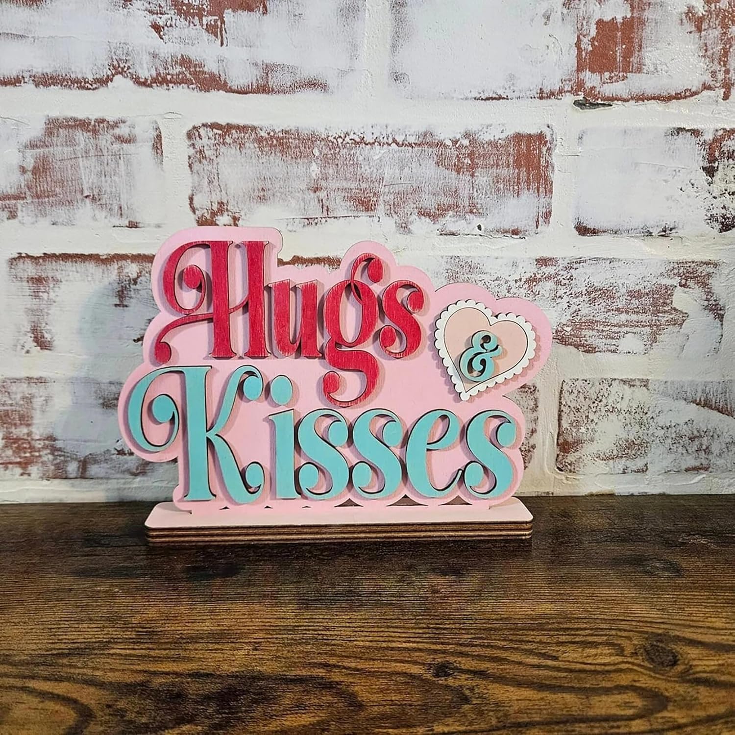 Decorative sign with 'Hugs & Kisses' text on a wooden surface and brick wall background