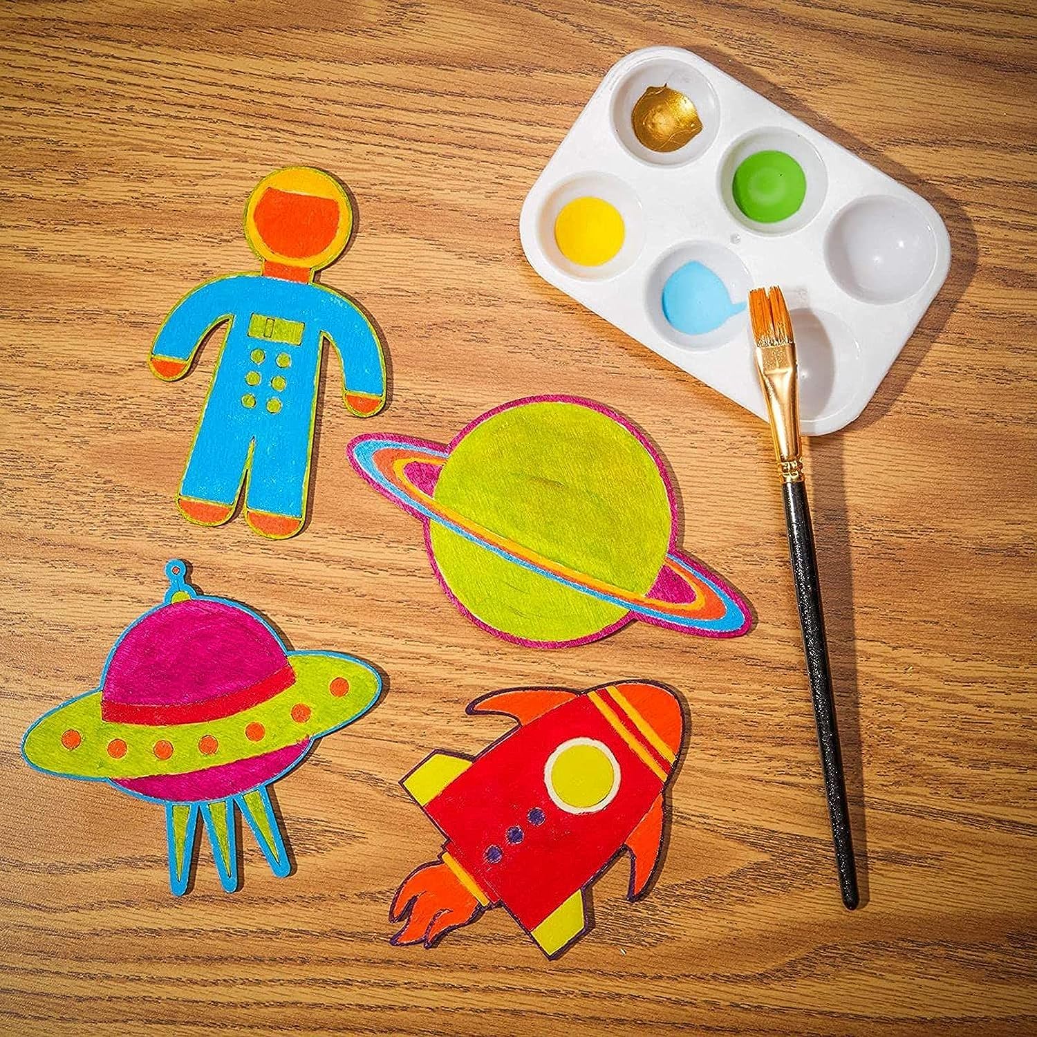 Colorful space-themed cutouts on a wooden surface with a paint palette and brush.